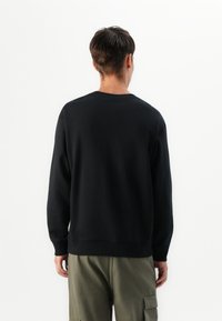 Black crew neck sweatshirt with long sleeves and ribbed cuffs. Features a relaxed fit, smooth texture, and is paired with olive cargo pants.