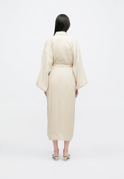 Μπεζ ρόμπα στυλ κιμονό με υφή σε διαμαντένιο σχέδιο, μακριά μανίκια και ζώνη στον ώμο. Μήκος μέχρι τη μέση της γάμπας.