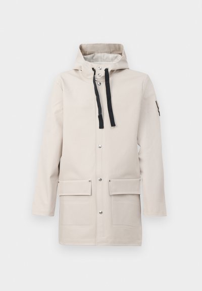 Chaqueta impermeable beige con capucha, que presenta cordones negros, botones a presión plateados y dos bolsillos frontales para almacenamiento.