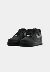 Black sneaker with rubber sole, smooth leather upper, perforated toe, gray accents, laces, and iconic logo on the tongue. Minimalist design.