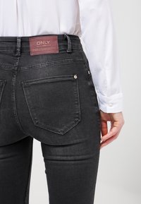 Jeans de mezclilla negra con un corte recto, que presentan una etiqueta de cuero marrón con la inscripción "ONLY" y dos bolsillos traseros con sutiles detalles de costura.