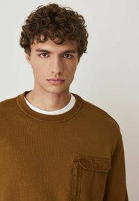 Sweatshirt din bumbac maroniu cu guler rotund, manșete ribbate și un buzunar pe piept cu nasture tip clapetă. Textură netedă și croială lejeră.