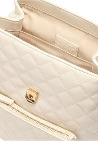Borsa tote in pelle sintetica crema trapuntata con una finitura in metallo dorato e una tasca frontale con zip. L'interno è foderato in tessuto beige.