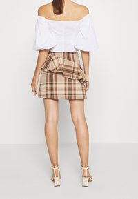 Biała bluzka bez ramiączek z bufkami zestawiona z beżową i brązową mini spódnicą w kratkę, z warstwowym detalem falbany oraz sandałami na słupku.