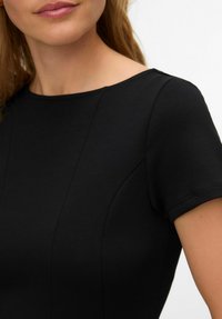 Melna kleita ar īsām piedurknēm un apaļu izgriezumu, ar gludu faktūru un smalkām šuvju detaļām uz krūtīm.