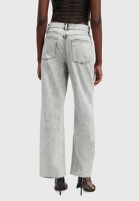 Jeans de tiro alto y pernera ancha en denim gris claro con un acabado desgastado. Presenta doble bolsillo trasero y dobladillos deshilachados, combinados con tacones negros.