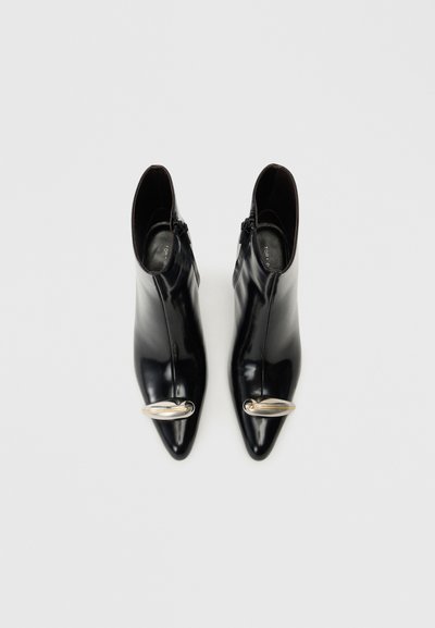 Black patent leather ankle boots with a pointed toe, featuring a gold accent on the front and a zipper on the outer side.