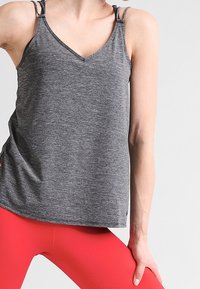 Szary sportowy top na ramiączkach z dekoltem w serek, cienkimi paskami i luźnym krojem, zestawiony z jaskrawoczerwonymi legginsami. Miękka faktura tkaniny.