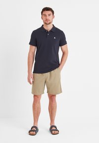 Navy polo shirt with a collar and short sleeves, paired with beige shorts. Sandals with dark straps on feet. Simple, casual outfit.
