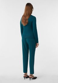 Turkusowy sweter i pasujące spodnie, wykonane z gładkiego materiału. Sweter ma dopasowany krój, a spodnie mają zwężane nogawki. Czarne buty na obcasie.