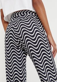 Pantalones de patrón en blanco y negro con rayas onduladas, cintura alta y textura suave, de ajuste ceñido y detalles de costura visibles.