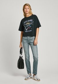 Black cropped t-shirt with colorful graphic and text, paired with light blue jeans. Accessorized with a black bag and silver sneakers.