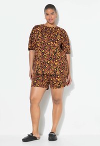 Bruine T-shirt met korte mouwen en korte broek set met een levendig geel en zwart bloem- en luipaardprintpatroon; gecombineerd met zwarte instapschoenen.