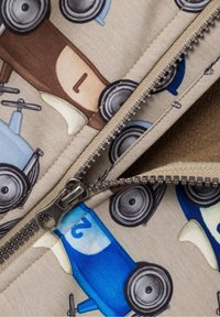 Tissu beige présentant des illustrations colorées de voitures-jouets en tons de bleu, marron et jaune. Fermeture éclair argentée et doublure beige douce visibles.