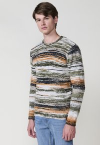Gestreepte gebreide sweater in groen, oranje en zwart met een textuurstof. Ronde hals en slim fit, gecombineerd met lichtblauwe denim jeans.