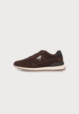 Baskets en daim marron foncé avec lacets, semelle blanche, semelle extérieure en gomme, accent noir au talon et logo Guess sur le côté.