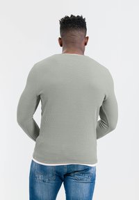 Langärmliges, geripptes Shirt in hellgrün mit rundem Halsausschnitt und strukturierter Oberfläche, kombiniert mit blauen Jeans.