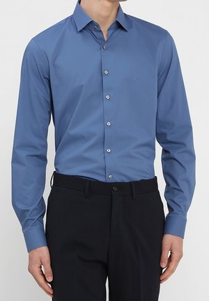 Niebieska, długosleeve koszula z rozłożonym kołnierzykiem, pięcioma guzikami z przodu oraz subtelnym logo na klatce piersiowej. Gładki materiał z dopasowanym krojem.