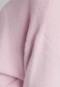 Tissu polaire rose pâle avec une surface douce et texturée, présentant des plis lisses et un léger éclat dans certaines zones.