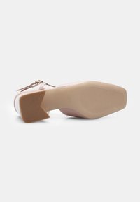 Pink heeled shoe with a textured upper, featuring a small strap and a wide, angular block heel. The sole is smooth with ridged patterns.