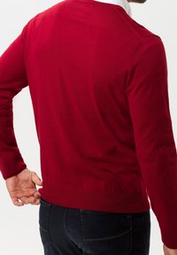 Pull rouge à col rond, manches longues et poignets côtelés. Texture lisse et coupe ajustée, assorti à un jean foncé.