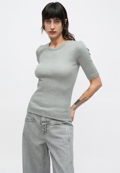 Γκρι ριμπ κοντομάνικη μπλούζα, στρογγυλή λαιμόκοψη, εφαρμοστή γραμμή, συνδυασμένη με ανοιχτό γκρι τζιν παντελόνι φαρδιάς γραμμής, με μπροστινές τσέπες και ξεθωριάσματα.
