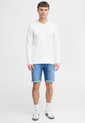 White long-sleeve V-neck shirt paired with blue denim shorts. The model wears white socks with black and gray shoes. Simple, casual outfit.