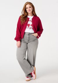 Veste bomber bordeaux, t-shirt graphique blanc, jeans gris à jambes larges et baskets roses avec des accents rouges. Tissus texturés et coupe décontractée.