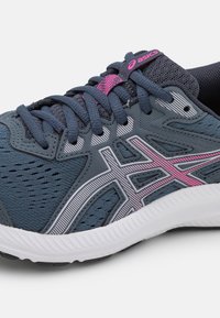 Chaussure de course avec un dessus en mesh bleu marine, accents gris clair et rose, design texturé et semelle en caoutchouc blanche. Comprend des lacets et un logo.