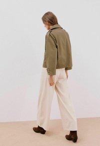 Oliwkowa, krótka kurtka z szerokim kołnierzem, zestawiona z kremowymi spodniami w szerokim kroju i brązowymi botkami za kostkę. Subtelna tekstura, brak widocznych wzorów.