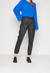 Blusa azul de manga larga con escote fruncido, combinada con pantalones negros ajustados y mocasines negros de suela gruesa. Tejido suave y textura lisa.
