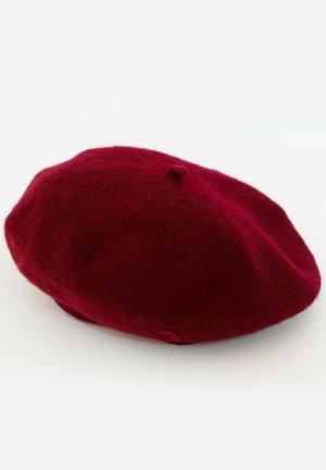Béret en laine bordeaux avec un sommet légèrement surélevé et une texture lisse, présentant un petit bouton au centre.