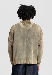 Light gold knitted sweater with a ribbed texture, oversized fit, and drop shoulders. Finished with wide, ribbed cuffs and hem.