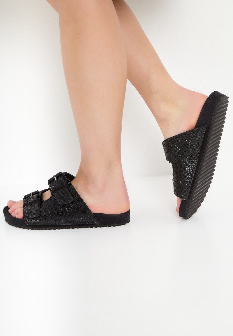 Zwarte slipper sandalen met een textuur van schuim aan de bovenkant, twee verstelbare gespen, een dikke rubberen zool en een geribbeld patroon aan de onderkant.