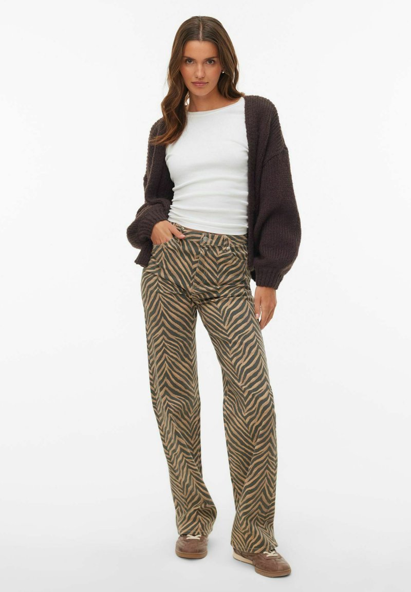 Brown knitted cardigan over a white shirt, paired with wide-leg pants featuring a tan and black zebra stripe pattern and flat shoes.