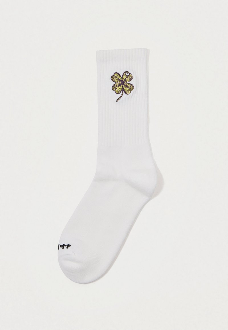 Biała skarpetka prążkowana z haftowanym u góry żółtym i brązowym koniczyną o czterech listkach oraz małym czarnym napisem na palcu.