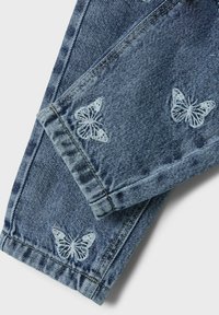 Jeans de mezclilla azul con mariposas blancas bordadas en el dobladillo. Las características incluyen un lavado desgastado, costuras visibles y piernas con vuelta.