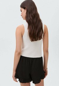 White ribbed sleeveless top paired with black ruffled shorts. The outfit features a textured fabric and a fitted design.