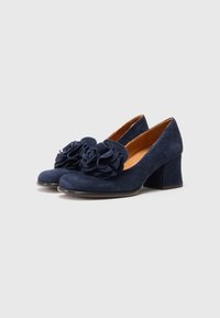 Navy blue suede heels with a rounded toe, featuring two large fabric flowers on the front and a sturdy block heel.