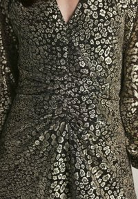 Robe noire et dorée avec un décolleté en V profond, taille froncée et motif léopard. Fabriquée en tissu texturé avec un éclat métallique.