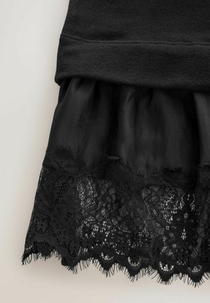 Czarna spódnica z koronkowym wykończeniem u dołu oraz marszczonym detalem materiału nad koronką na neutralnym tle.