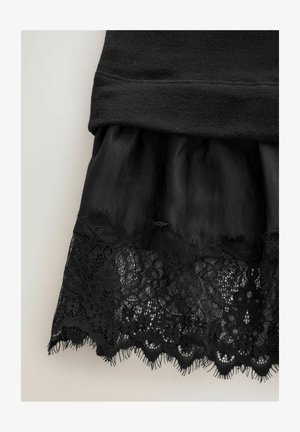 Czarna spódnica z koronkowym wykończeniem u dołu oraz marszczonym detalem materiału nad koronką na neutralnym tle.