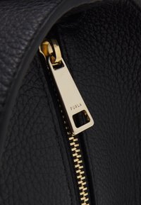 Svart läderväska med en guldfärgad dragkedja och en etikett märkt "FURLA" samt synliga tänder, som visar en texturerad yta.