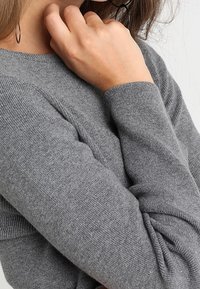 Grå strikket sweater med rund hals og lange ærmer med ribbede manchetter, der viser en blød tekstur og afslappede designdetaljer.