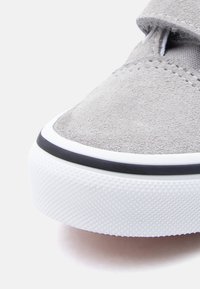 Αθλητικό παπούτσι από γκρι σουέντ με λεία υφή, λευκή λαστιχένια σόλα και μαύρο περίγραμμα. Διαθέτει ιμάντα με βέλκρο για ασφαλή εφαρμογή.