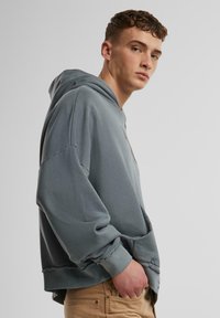 Gray oversized hoodie with a drawstring, ribbed cuffs, and a hem with frayed detailing. Pockets on both sides. Soft cotton blend material.