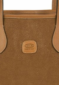 Helle Lederhandtasche mit strukturierten Oberflächen, zwei Griffen und einem dekorativen Etikett. Verfügt über beige Nähte und ein rechteckiges Etikett mit dem Prägung "BRICS Made in Italy."