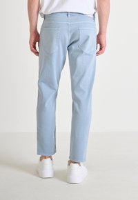Pantalones de mezclilla azul claro con pierna recta, con dos bolsillos traseros y una cintura, combinados con zapatillas blancas. Tejido texturizado.