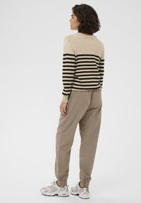 Stribet sweater i beige og sort, kombineret med lysebrune joggingbukser. Fodtøj med gråt og hvidt design med detaljer.