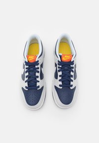 Paire de baskets Nike bleu marine et blanc avec logo Nike orange sur semelles intérieures jaunes, vues de dessus sur fond blanc.